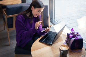 Uma mulher concentrada navega em um site de e-commerce pelo notebook, analisando produtos e comparando preços. A imagem transmite praticidade, confiança e a experiência fluida de compra online, elementos que refletem o crescimento do comércio digital no Brasil.
