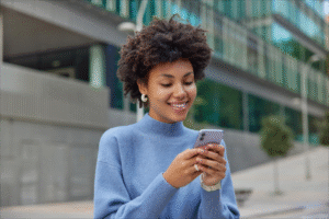 Mulher jovem sorrindo enquanto mexe no celular, representando conexão emocional entre marcas e consumidores por meio de campanhas alinhadas a valores.