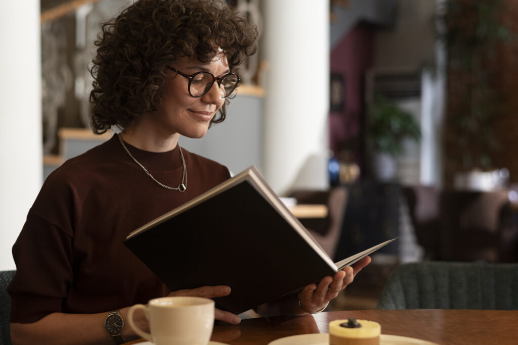 mediumshotwomanreadingmenu AnonMedia Mulher sentada lendo um livro de marketing representando aprendizado e desenvolvimento estratégico para crescimento de marcas
