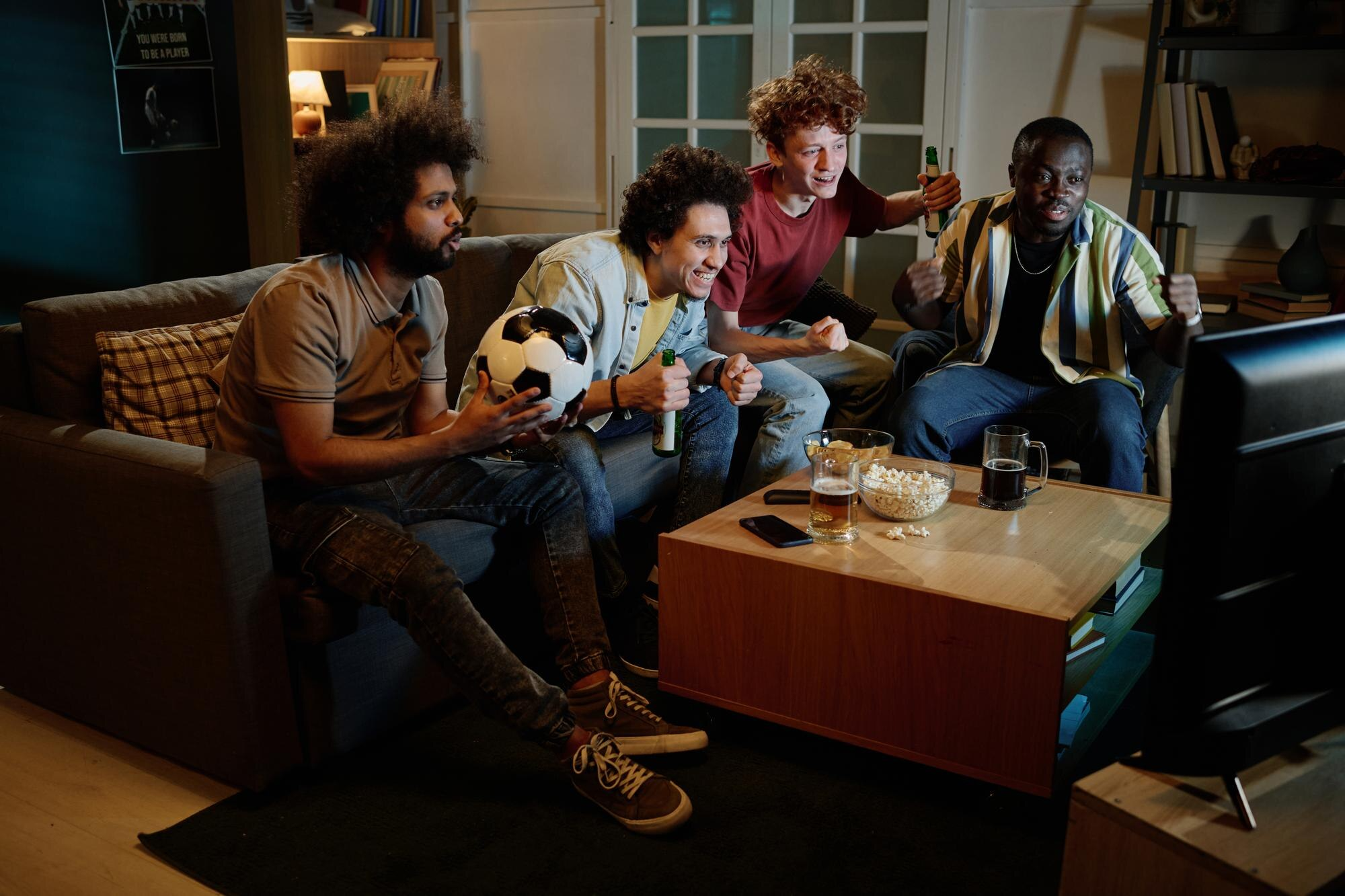 Grupo de amigos assistindo a um jogo de futebol da Copa, com bebidas e petiscos, aproveitando o momento de confraternização, ilustrando o "efeito partida" que impulsiona as vendas no varejo durante os jogos do Brasil.